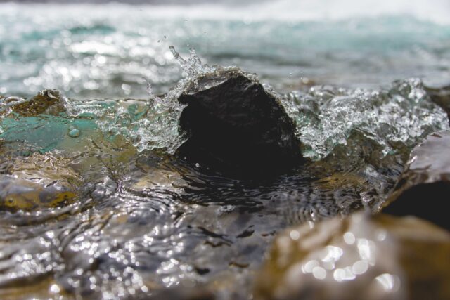 selective focus photography of water crashing on black stone