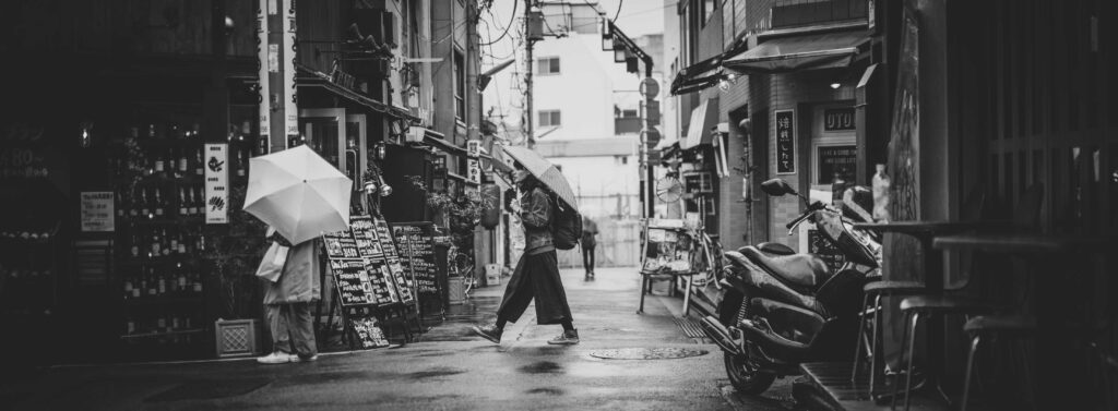 grayscale photo of man in black coat walking on street