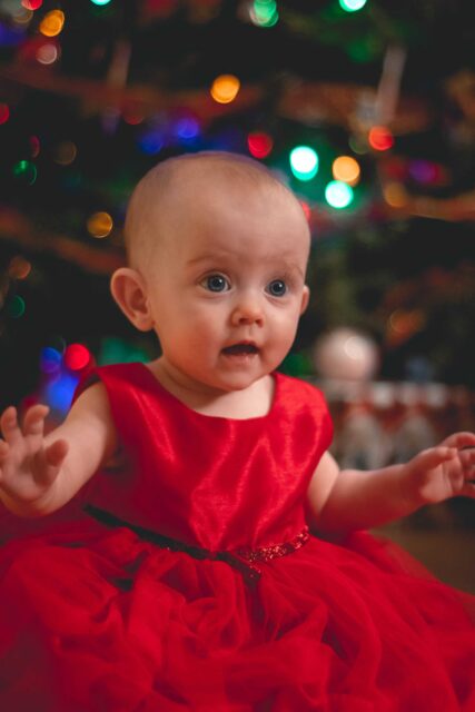 child in red satin dress by Christmas tree