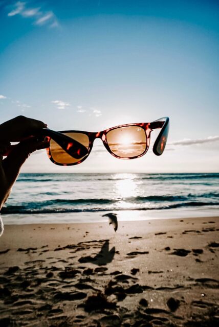 person holding sunglasses on beach during daytime