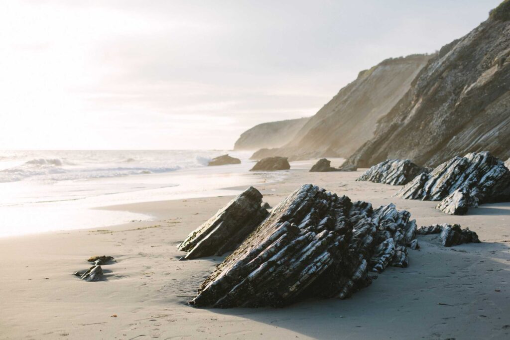 brown rock formation on white sand beach during daytime