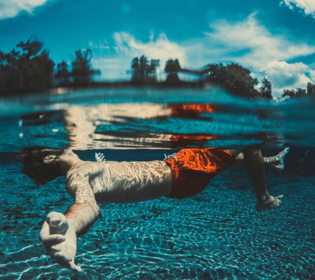 underwater photography of floating man wearing red shorts